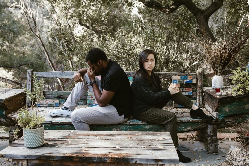 Two people sitting back-to-back in silence, each looking distressed, symbolizing the emotional disconnection that can result from people-pleasing in relationships.