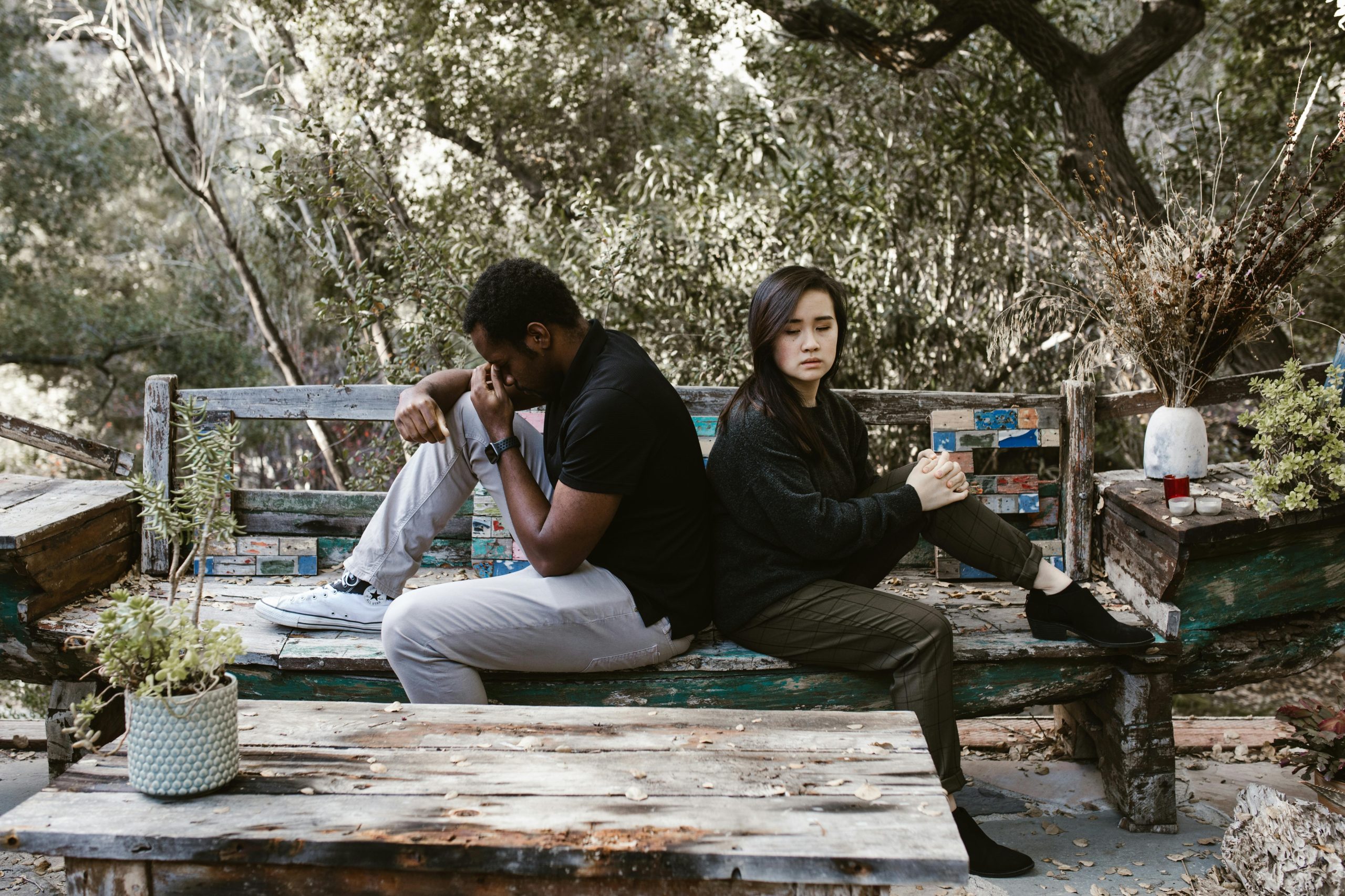 Two people sitting back-to-back in silence, each looking distressed, symbolizing the emotional disconnection that can result from people-pleasing in relationships.