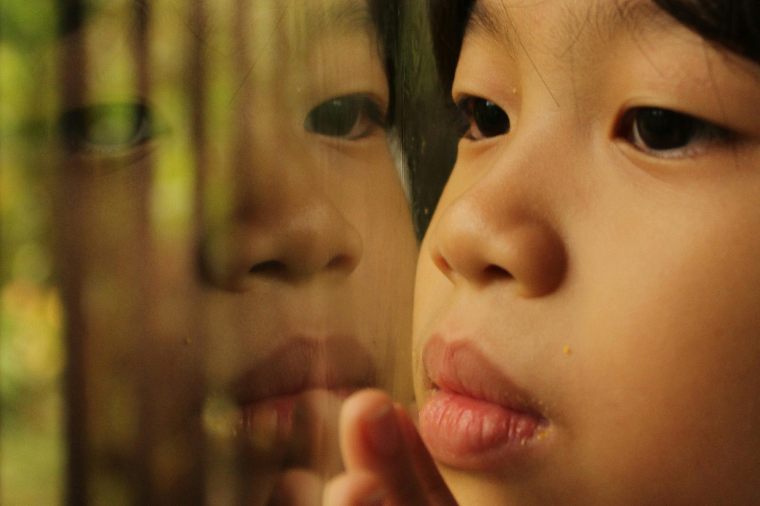 Child gazing out a window with a soft reflection, symbolizing early emotional sensitivity and the roots of people-pleasing behavior.