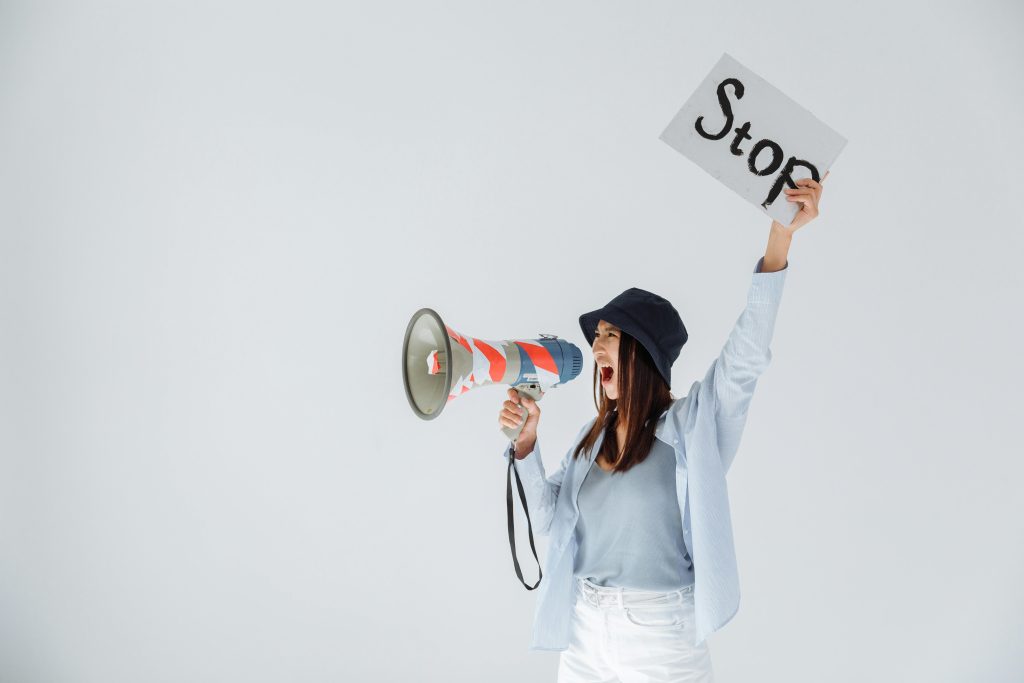 A woman holding a megaphone and a sign that says “Stop,” shouting with determination—symbolizing the act of reclaiming one’s voice and setting boundaries.