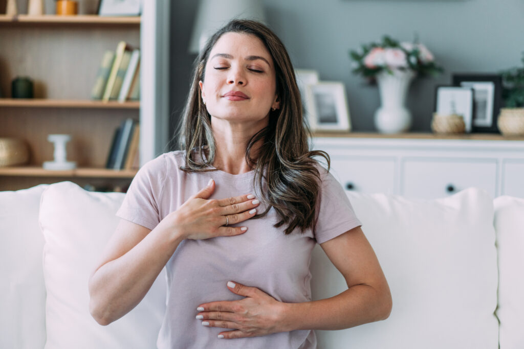 A woman with her hand on her chest and eyes closed, reflecting how trauma and PTSD therapy supports the body and nervous system in feeling safe again.