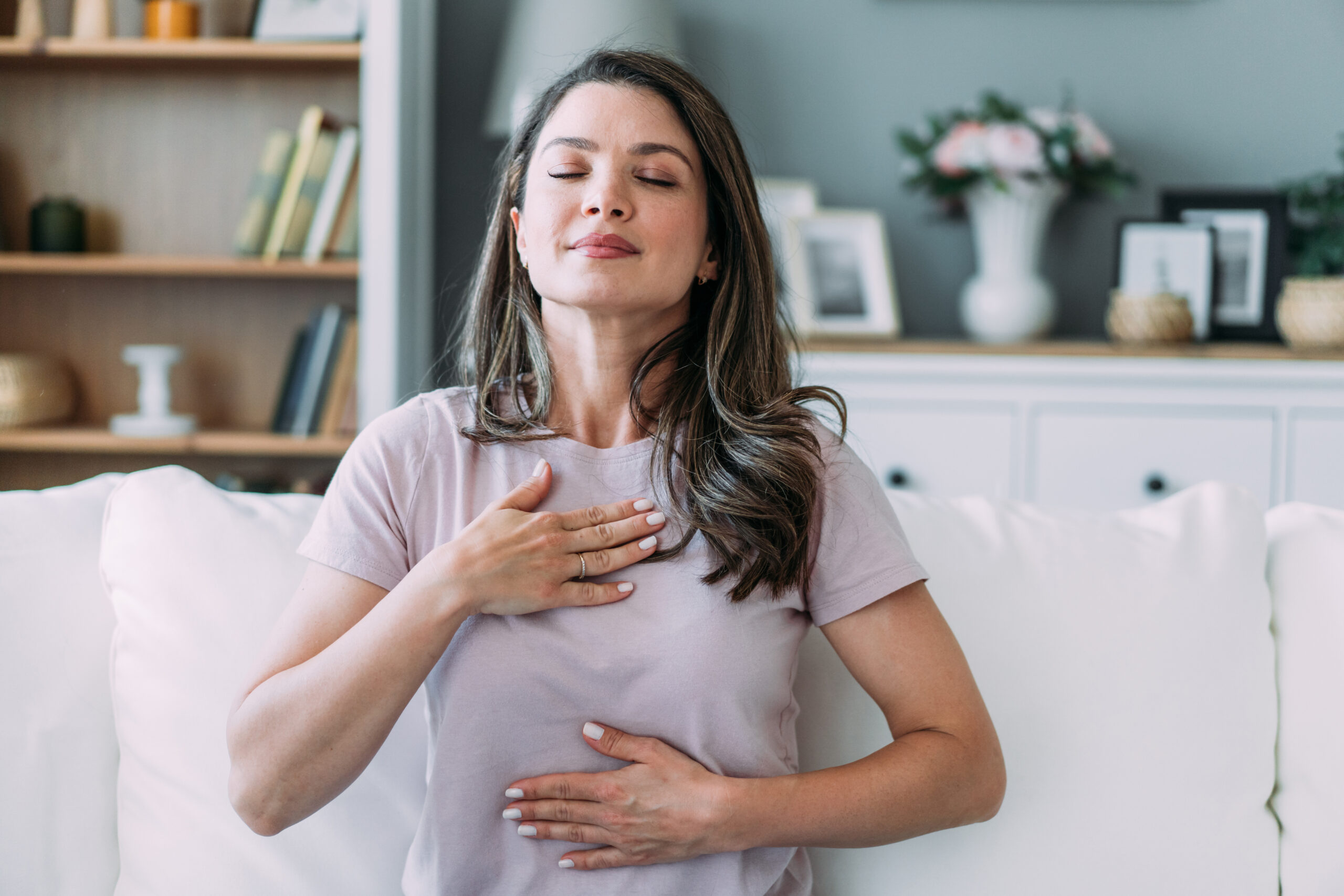 A woman with her hand on her chest and eyes closed, reflecting how trauma and PTSD therapy supports the body and nervous system in feeling safe again.