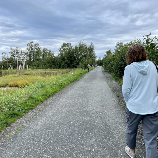 A person walking slightly behind others on a wide path, reflecting what it feels like when connection is desired but still feels uncertain or risky.