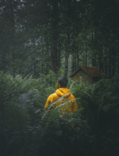 A person in a yellow jacket standing still on a forest path, reflecting the hesitation and inner tension of wanting to speak but holding back.
